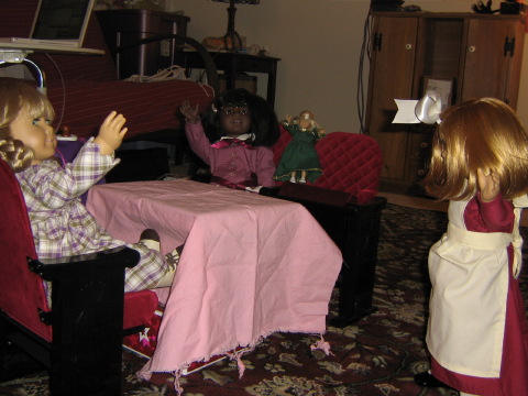 Nellie looks back to see Kirsten, Pegleg Sally, May, and Mini Kit sitting at a table draped in a pink tablecloth.