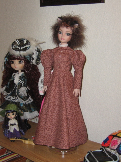 Pink 1890s-inspired calico dress on an Ellowyne doll with a feather wig and cat ears; Veritas Pullip (pirate captain looking doll) in background with purple-haired mini Pullip