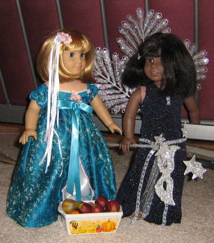 Nellie (same dress) and May (in a fancy navy-blue sequined dress with a silver "peacock" tail) stand in front of a bin of pumpkins and apples.