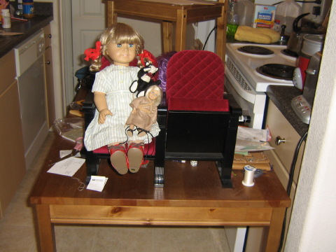 Kirsten, Mini Kit, and May's cat sit on a theater seat on the table in the kitchen.